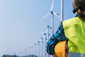Woman engineer in uniform and holding yellow safety helmet with standing and checking wind turbine power